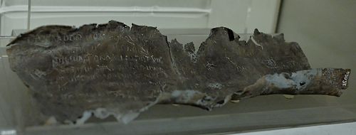 Photo of an ancient crumbling tablet of lead (metal) with writing etched into it.